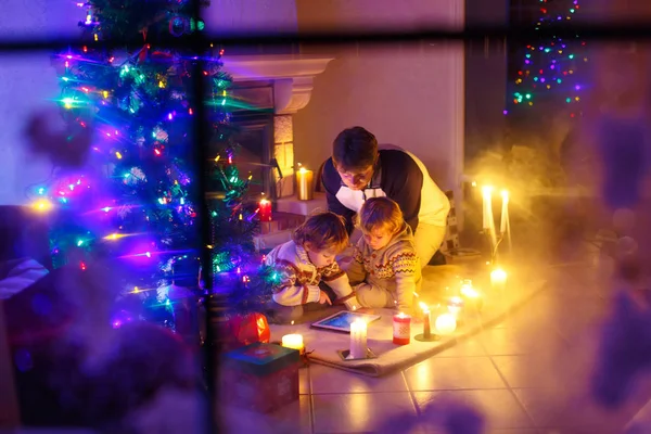Far och hans två små barn sitter av eldstad skorsten på julafton tid. — Stockfoto