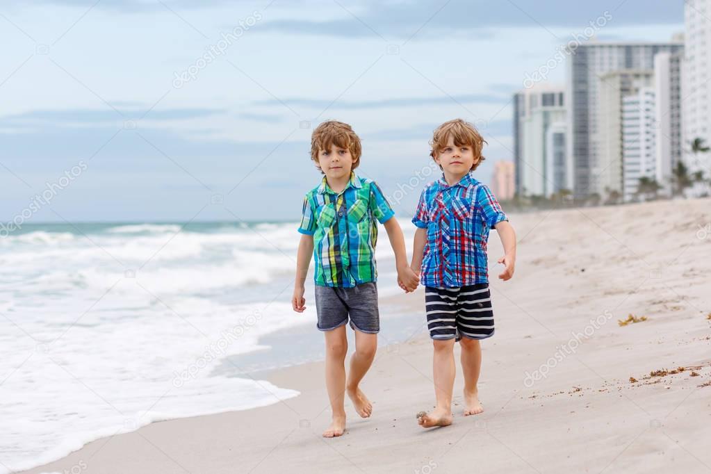 Two little kids boys running on the beach of ocean