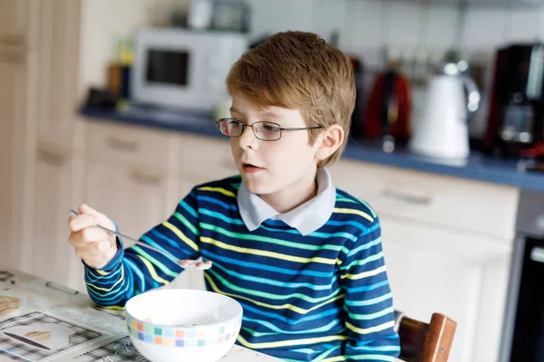 Szczęśliwy mały chłopiec blond dziecko jeść płatki na śniadanie lub lunch. Zdrowe jedzenie dla dzieci. — Zdjęcie stockowe