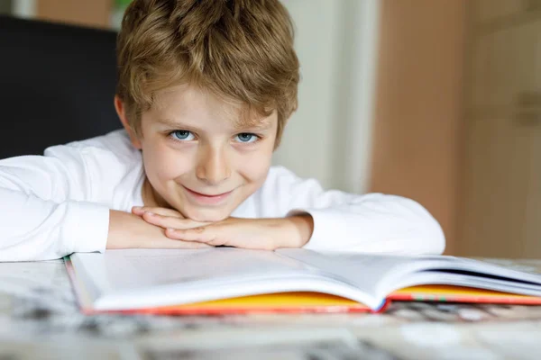 Liten blond skola unge pojke en bok hemma — Stockfoto