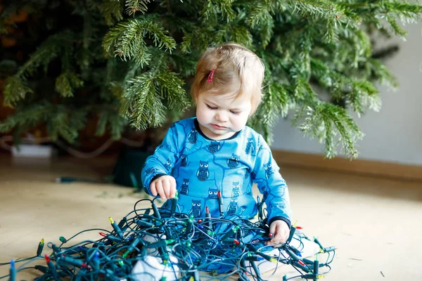 Nettes kleines Mädchen, das die Weihnachtsdekoration vom Christbaum abnimmt. Kind mit Lichterkranz. — Stockfoto