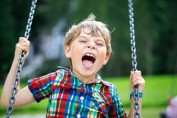 Funny kid boy having fun with chain swing on outdoor playground during rain — Stock Photo, Image