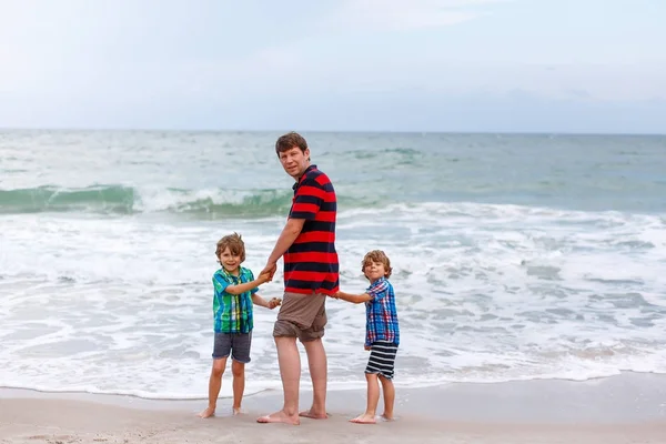 Dvě malé děti chlapci a otec na pláži oceánu — Stock fotografie