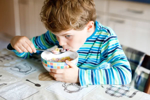 Bedårande liten blond skola unge pojke äter flingor med mjölk och bär till frukost eller lunch. — Stockfoto