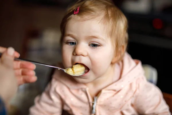 Entzückendes kleines Mädchen, das aus einem Löffel püriertem Gemüse und Püree isst. Ernährungs-, Kinder-, Ernährungs- und Personenkonzept — Stockfoto