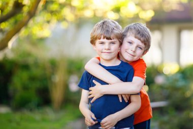 Two little active school kids boys, twins and siblings hugging on summer day clipart