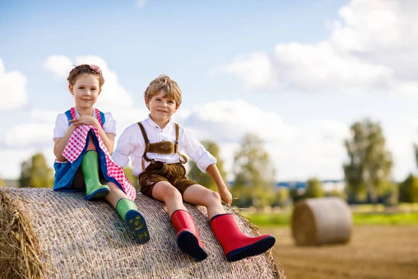 Adorable niño y niña en trajes tradicionales bávaros en el campo de trigo en la pila de heno —  Fotos de Stock