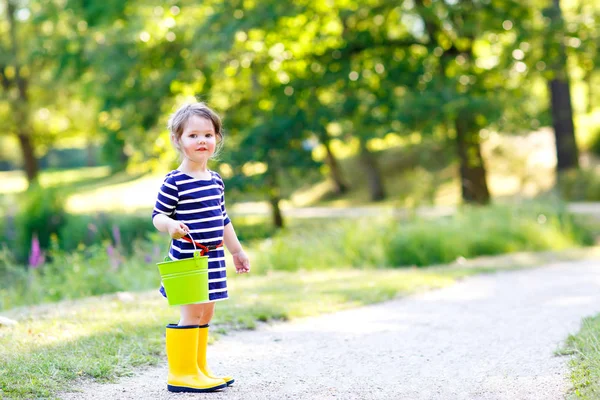 Beautiful little toddler girl playing in park. Adorable child wearing fashion casual clothes and yellow rubber boots. — Stock Photo, Image