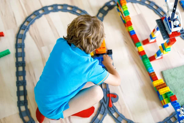 Liten blond unge pojke leker med färgglada plast block och skapa tågstation — Stockfoto