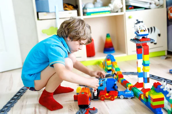 Pequeño niño rubio jugando con bloques de plástico de colores y la creación de la estación de tren —  Fotos de Stock