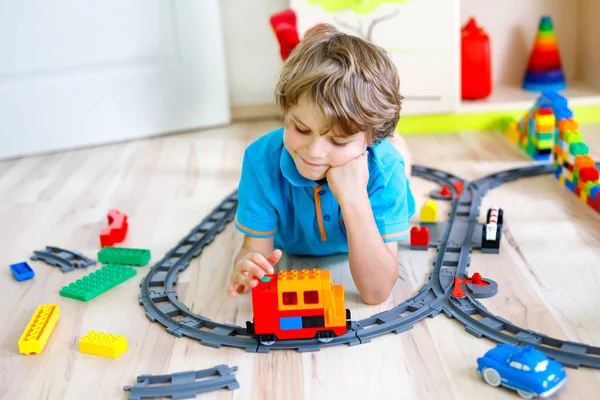 Szőke kisgyerek fiú játszani a színes műanyag blokkokat és megteremti a vasútállomás — Stock Fotó