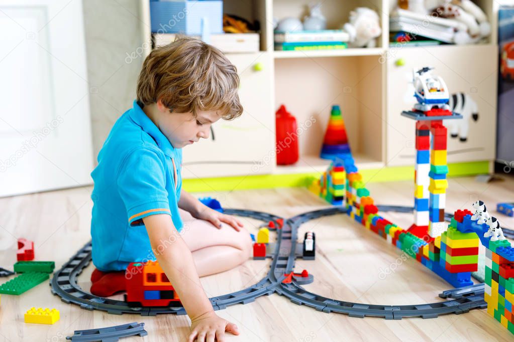 little blond kid boy playing with colorful plastic blocks and creating train station