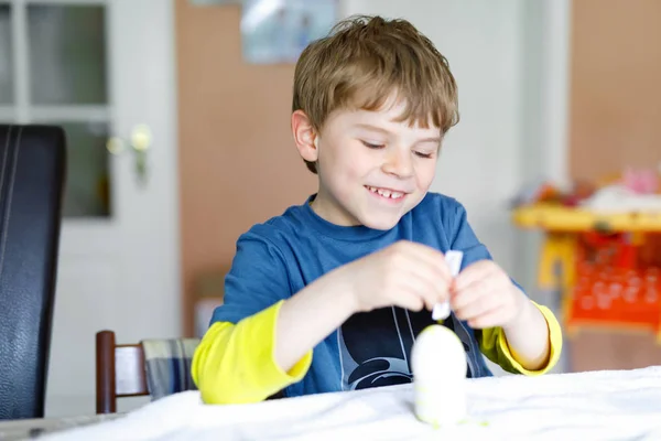 Little blond kid boy coloring eggs for Easter holiday in domestic kitchen, indoors. — Stock Photo, Image