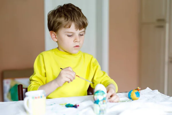 Μικρό παιδί ξανθό αγόρι αυγά χρωματισμό για διακοπές το Πάσχα στην εγχώρια κουζίνα, σε εσωτερικούς χώρους. — Φωτογραφία Αρχείου