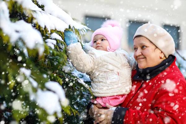 Vackra mormor håller baby flicka i barnvagn under snöfall på vintern — Stockfoto