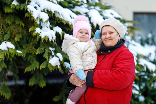 美しい祖母乳母車の冬の降雪の中に女の赤ちゃんを保持 — ストック写真