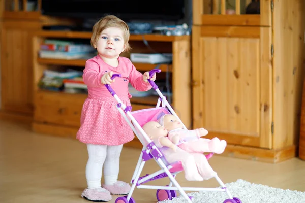Bonito adorável bebê menina fazendo primeiros passos com boneca carruagem . — Fotografia de Stock