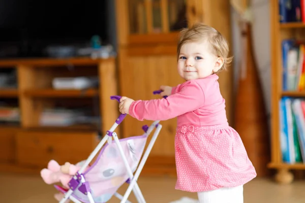 Schattige schattig babymeisje eerste stappen met pop vervoer. — Stockfoto