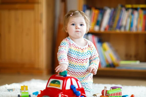 Schattig leuk mooie babymeisje spelen met houten onderwijsspeelgoed thuis of kwekerij. Peuter met kleurrijke rode auto — Stockfoto