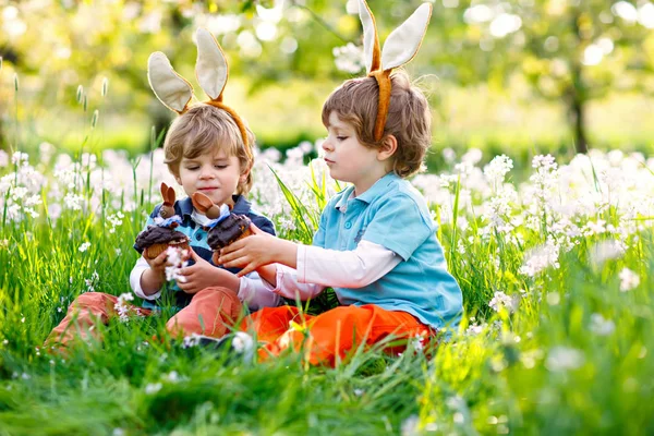 Zwei kleine Freunde in Osterhasenohren essen Schokoladenkuchen und Muffins — Stockfoto