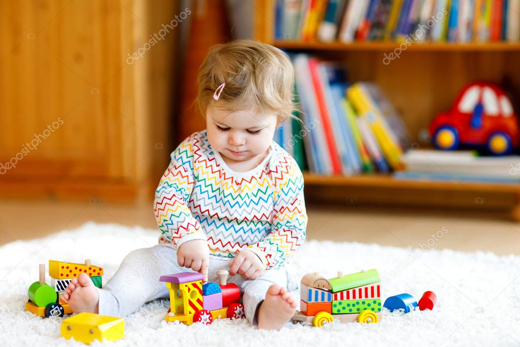 Adorable cute beautiful little baby girl playing with educational wooden toys at home or nursery. Toddler with colorful train