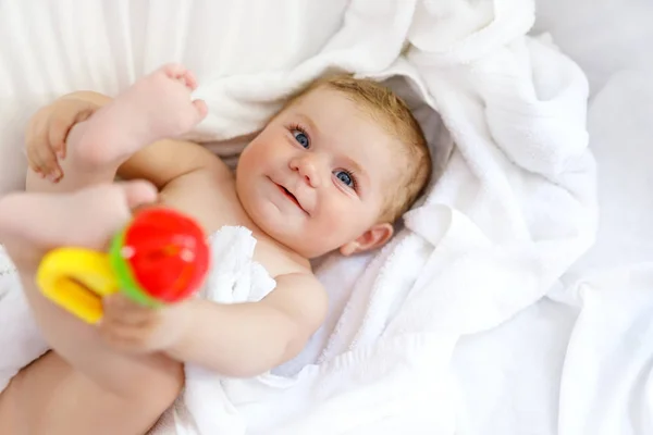 Bebé bonito brincando com chocalho de brinquedo e próprios pés depois de tomar banho. Adorável menina bonita envolto em toalhas brancas — Fotografia de Stock