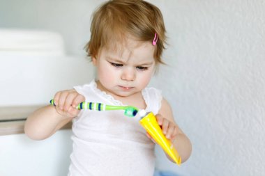 Küçük kız diş fırçası tutuyor ve ilk dişlerini fırçalıyor. Bebek süt dişini temizlemeyi öğreniyor..