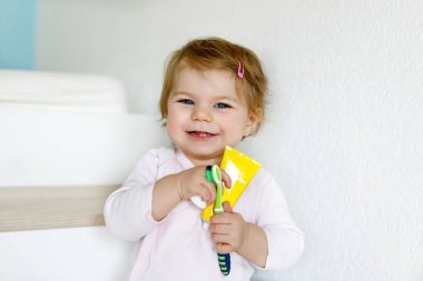 Küçük kız diş fırçası tutuyor ve ilk dişlerini fırçalıyor. Bebek süt dişini temizlemeyi öğreniyor..