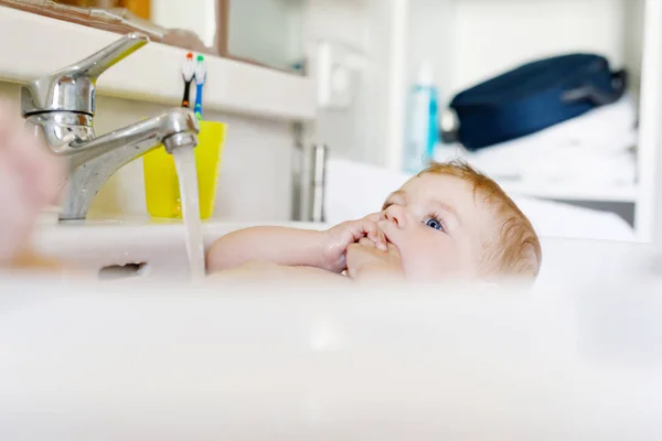 可爱可爱的宝宝，考虑在洗涤池浴和抢水龙头. — 图库照片