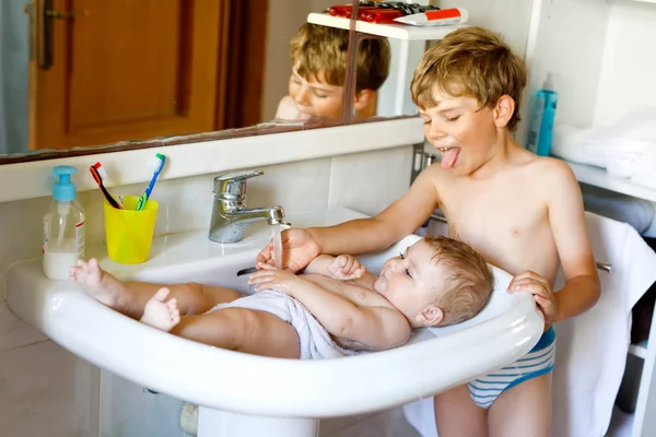Niedliches entzückendes Baby badet in Waschbecken und schnappt sich Wasserhahn. — Stockfoto