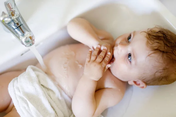 Bebê adorável bonito tomando banho na pia de lavagem e pegar torneira de água . — Fotografia de Stock