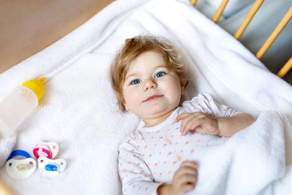 Cute little baby girl holding bottle with formula mild and drinking. Child in baby cot bed before sleeping — Stock Photo, Image