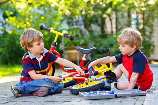 Zwei glückliche kleine Jungen reparieren Kette auf Fahrrädern und wechseln Rad des Laufrads — Stockfoto