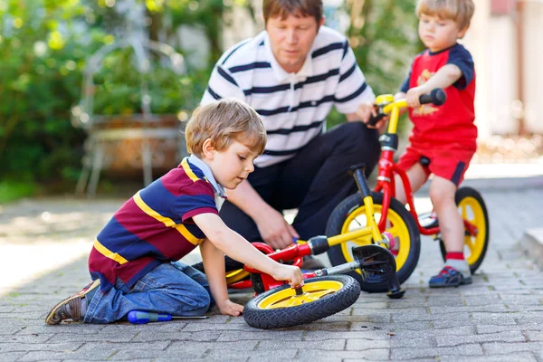 Zwei glückliche kleine Jungen und Vater reparieren Kette auf Fahrrädern und wechseln Rad des Laufrades — Stockfoto