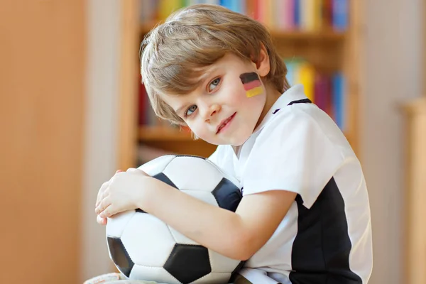 Kleine blonde kleuter jongen met bal kijken voetbal cup wedstrijd op tv. — Stockfoto