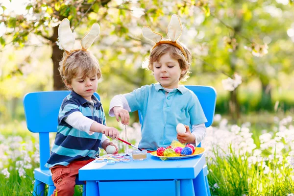 Two little boys wearing Easter bunny ears, painting colorful egg — Stock Photo, Image