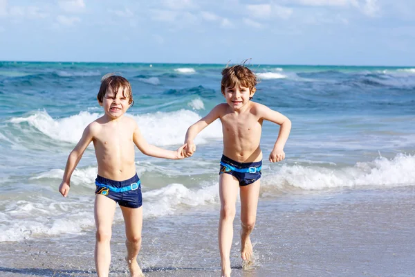 Due ragazzini che corrono sulla spiaggia dell'oceano. Bambini piccoli che si divertono — Foto Stock