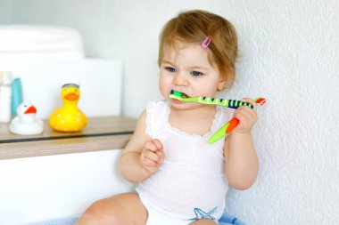 Küçük kız diş fırçası tutuyor ve ilk dişlerini fırçalıyor. Bebek süt dişini temizlemeyi öğreniyor..