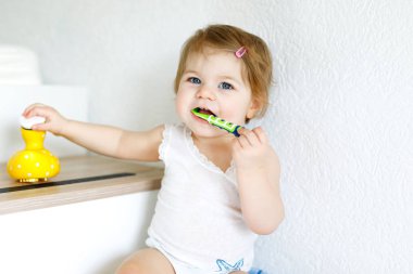 Küçük kız diş fırçası tutuyor ve ilk dişlerini fırçalıyor. Bebek süt dişini temizlemeyi öğreniyor..