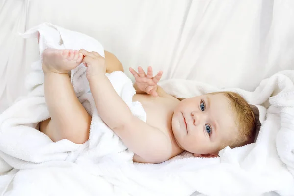 Мила маленька дитина грає з власними ногами після прийняття ванни. Чарівна красива дівчина, загорнута в білі рушники — стокове фото