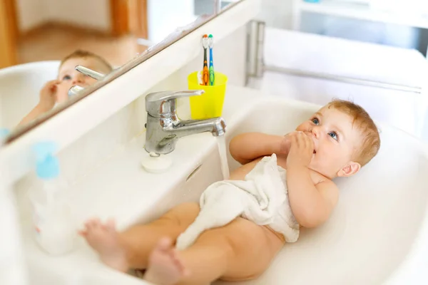 Cute adorable baby taking bath in washing sink and grab water tap. — Stock Photo, Image