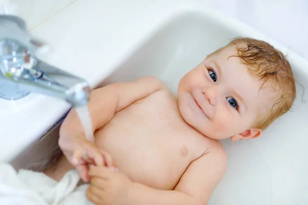 Schattige schattig baby nemen bad in wassen gootsteen en waterkraan pak. — Stockfoto