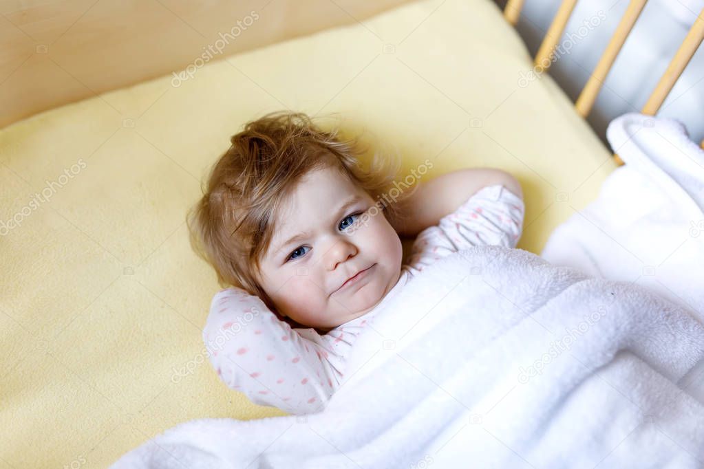 Cute little baby girl lying in cot before sleeping. Happy calm child in bed. Going sleep. Peaceful and smiling child
