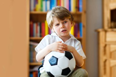 Futbolu ya da futbol maçını kaybettiği için üzgün ve mutsuz küçük bir çocuk. TV 'de maç izledikten sonra çocuk