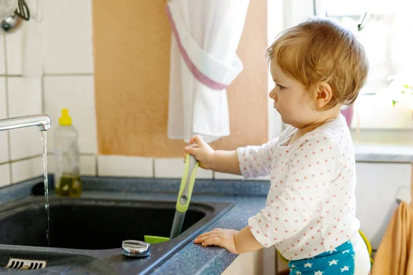 Manis gadis kecil pirang mencuci piring di dapur domestik. — Stok Foto