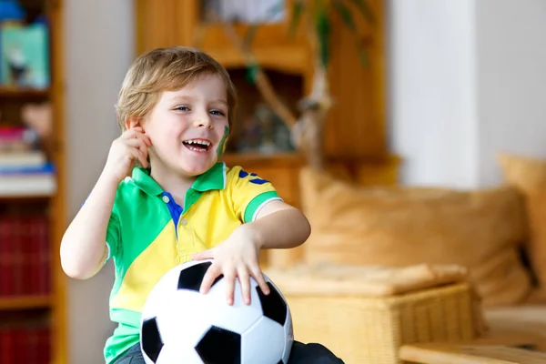 Kleine blonde kleuter jongen met bal kijken voetbal cup wedstrijd op tv. — Stockfoto