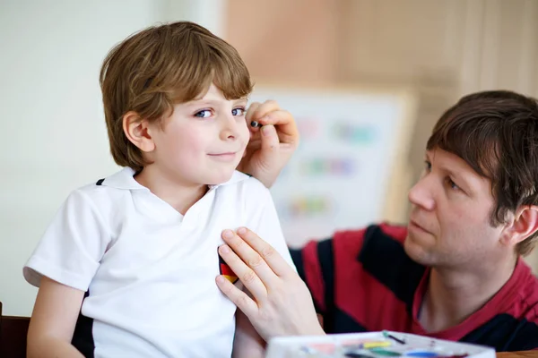 Young dad painting flag on face of little son for football or soccer game. — Stock Photo, Image