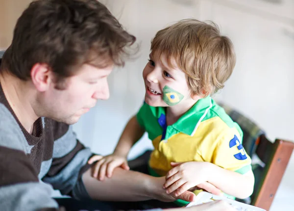 Young dad painting flag on face of little son for football or soccer game. — Stock Photo, Image