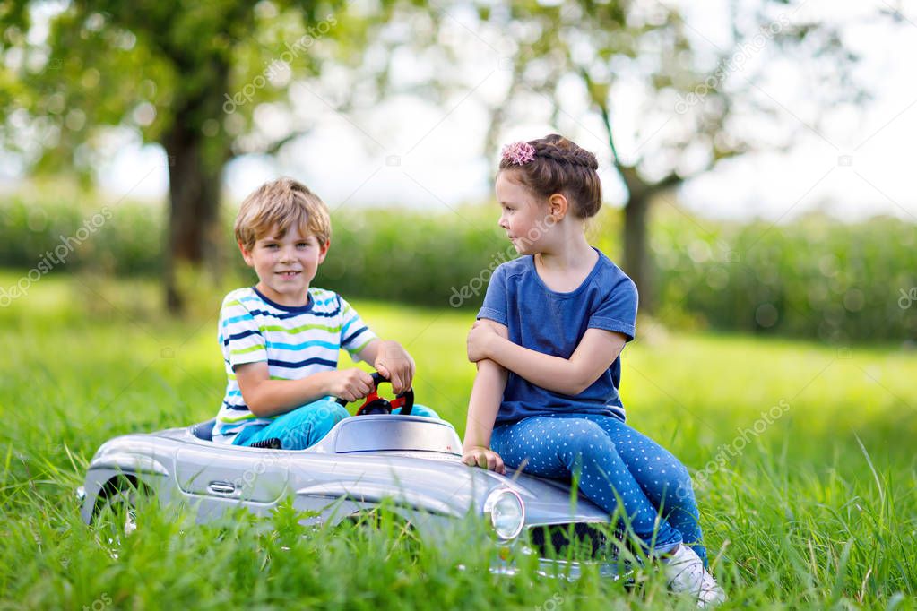 Two happy children playing with big old toy car in summer garden, outdoor