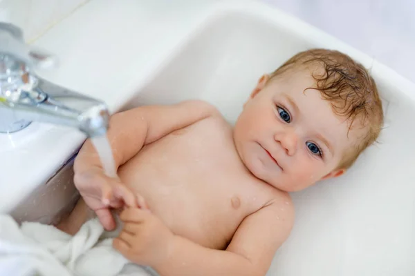 Lindo adorable bebé tomando baño en lavado lavabo y agarrar agua grifo . —  Fotos de Stock